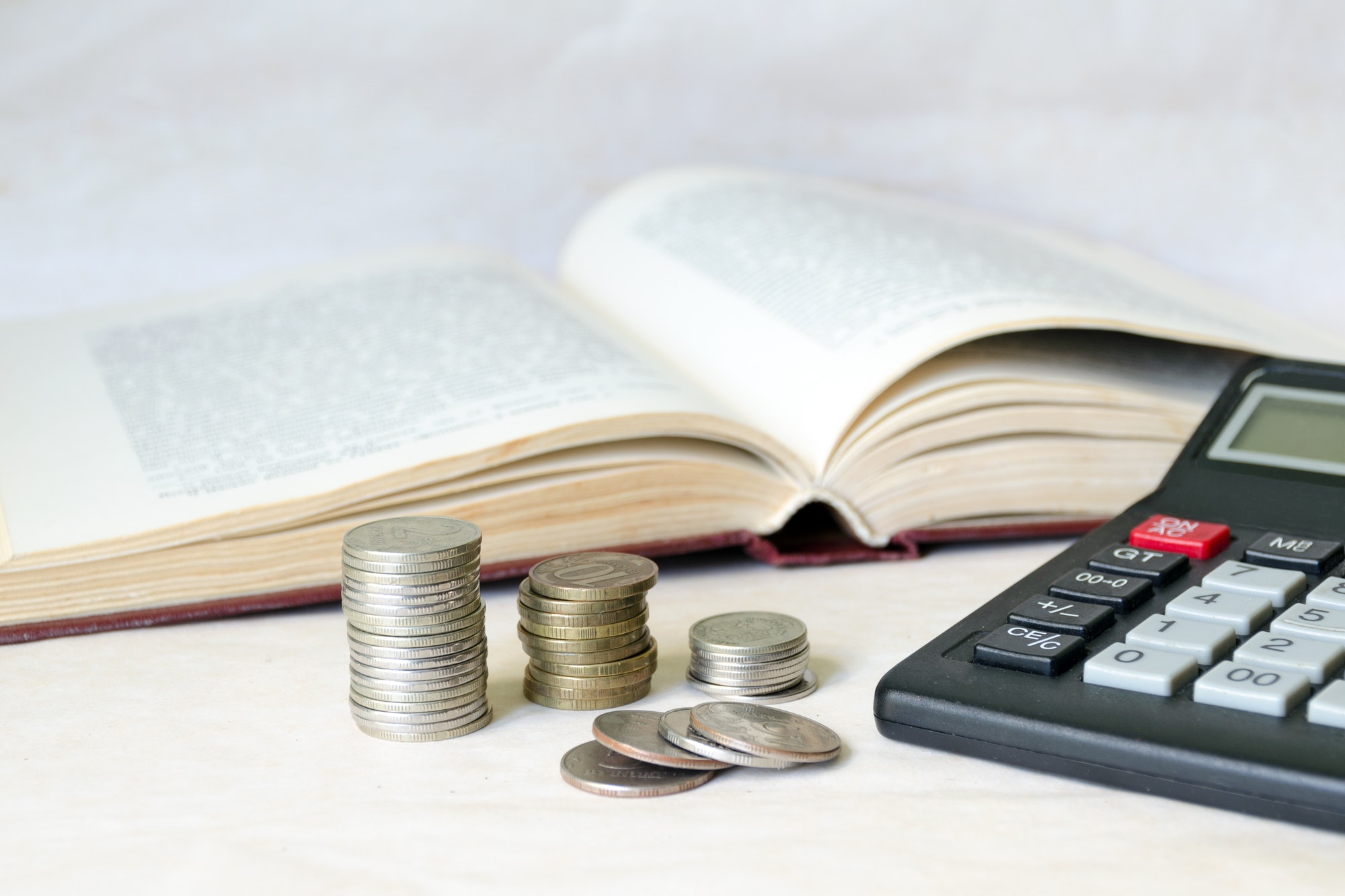 a stack of coins and a calculator in front of an open book