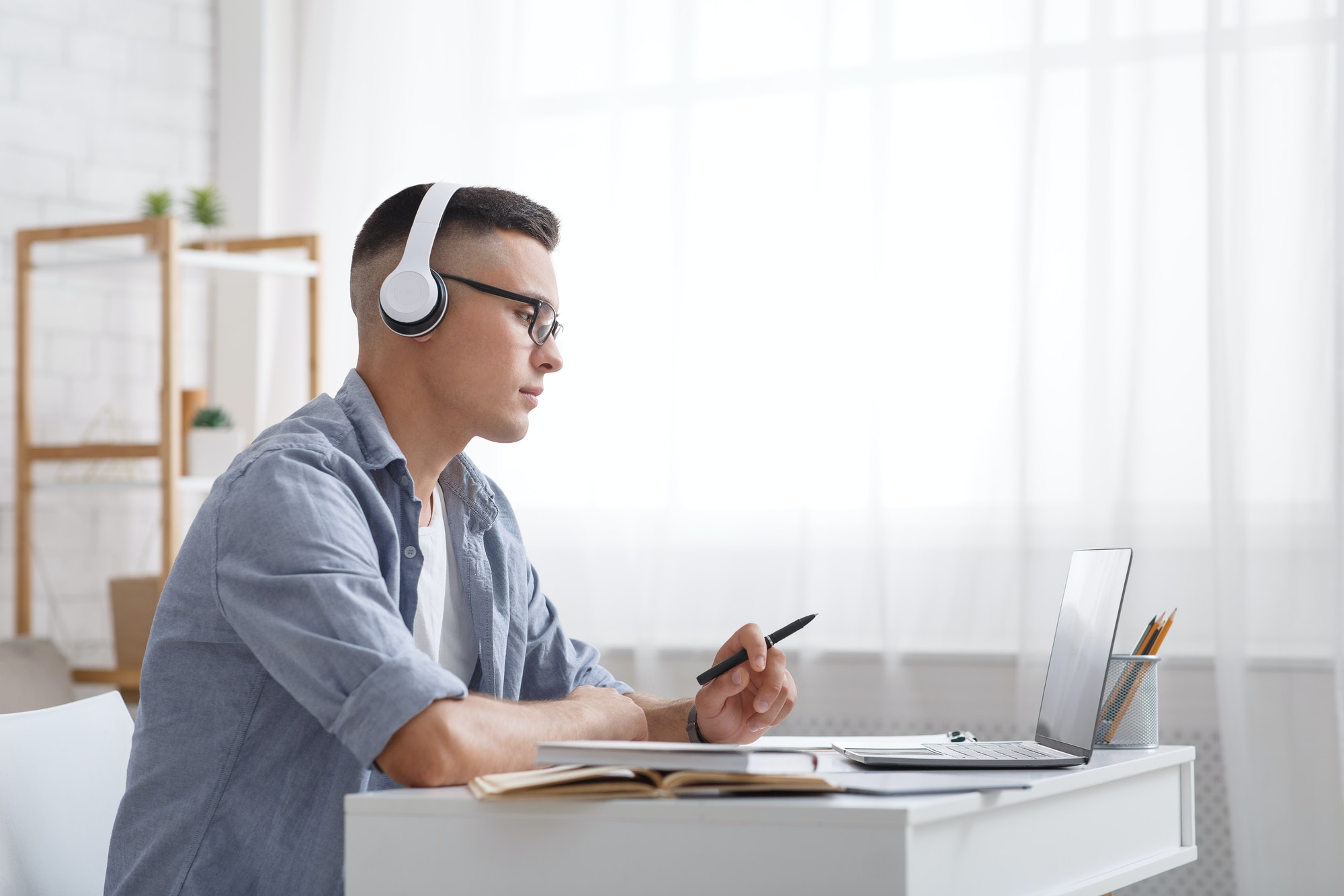 online education and work at home young man in headphones holds pen and looks at laptop sitting at