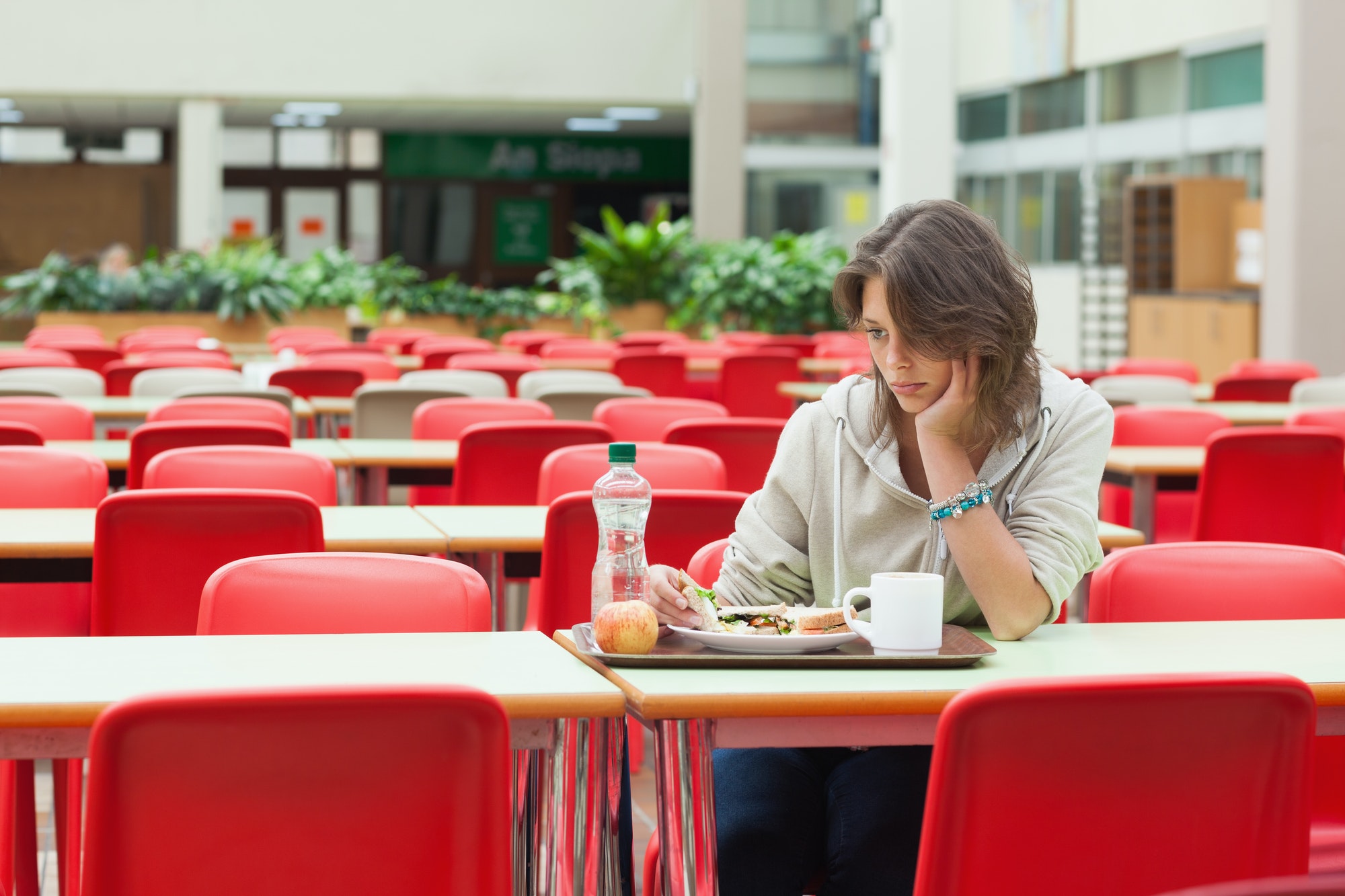 alone and sad female student sitting in the cafeteria with food tray
