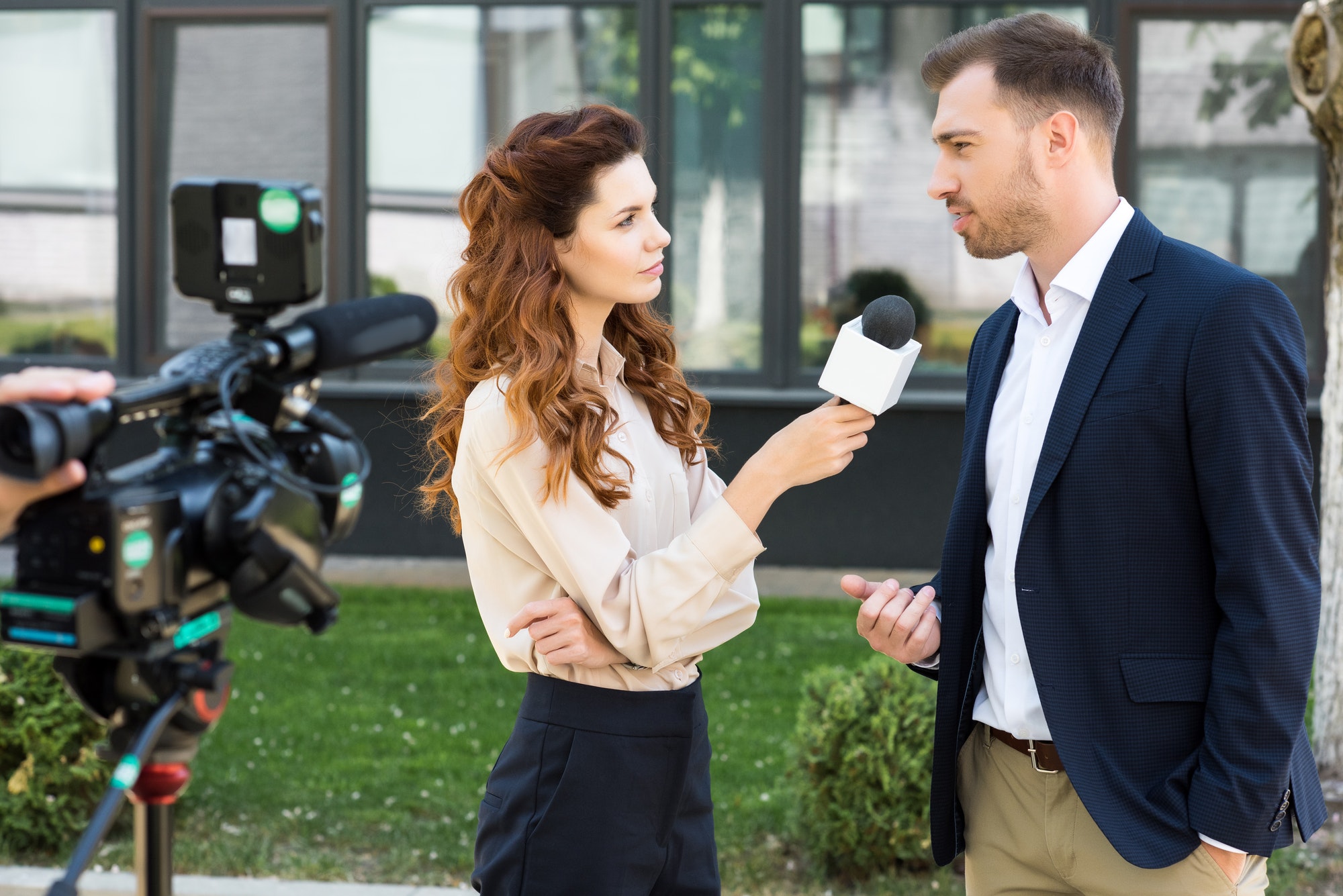 beautiful serious female news reporter taking interview with businessman