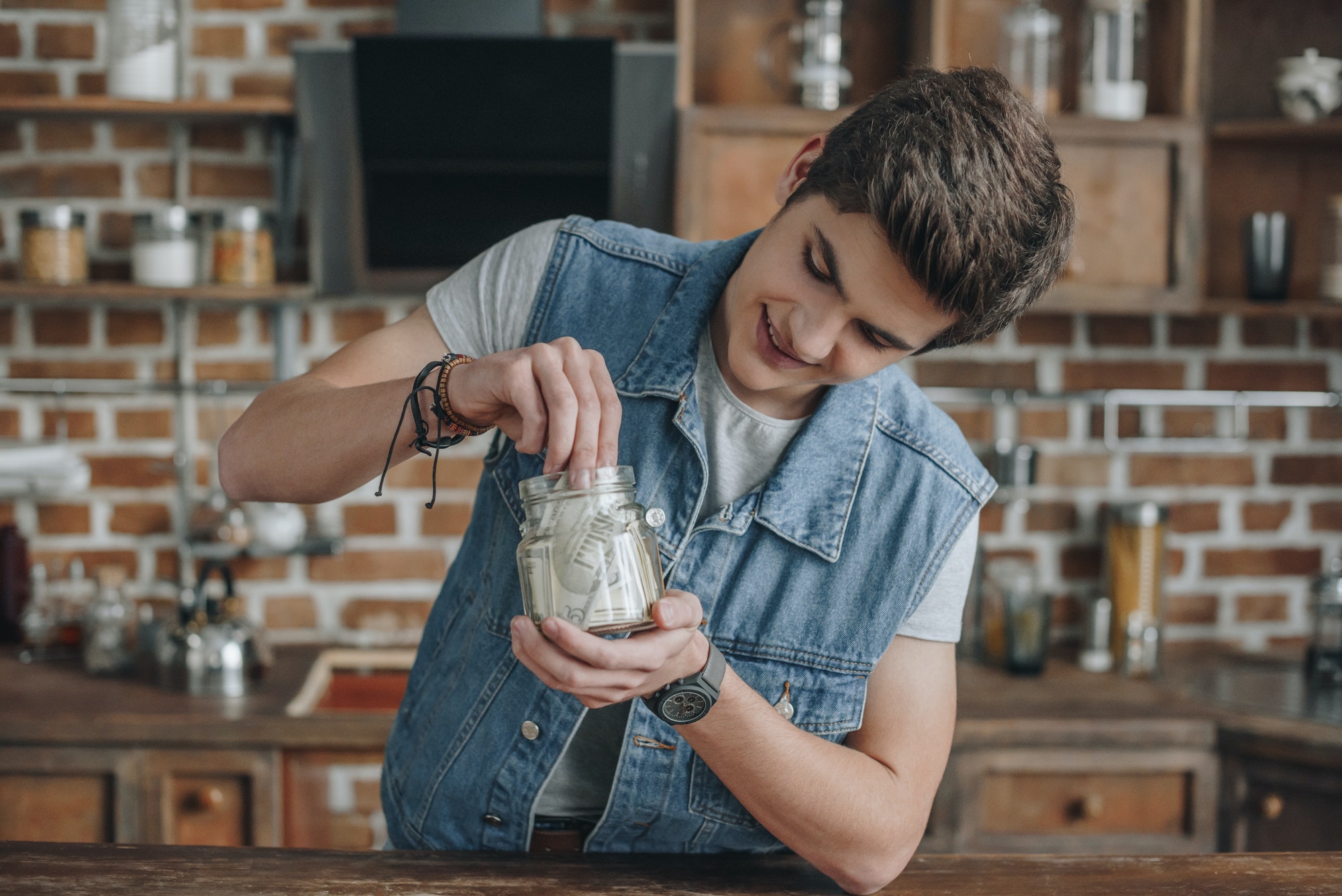 smiling teenager taking dollar banknotes from saving glass jar for money