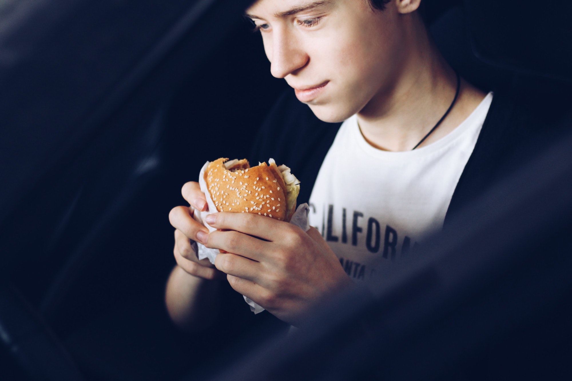 The young man eats hamburger in the car
