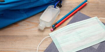 Sanitizer gel, medical mask and school supplies on a student desk