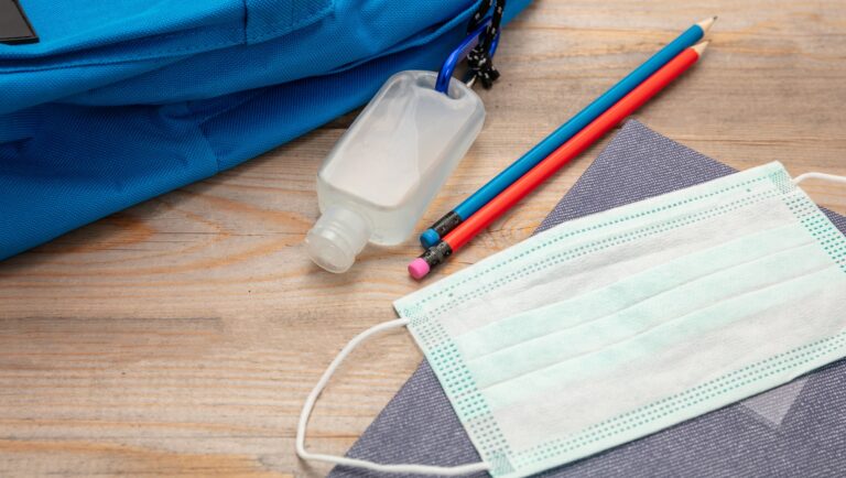 Sanitizer gel, medical mask and school supplies on a student desk