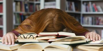 Tired redhead girl sleeping on books at campus library