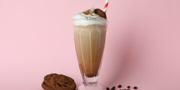 glass of milkshake coffee seeds and cookies on pink background