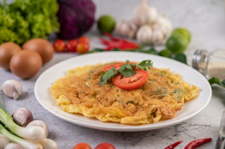 Omelet in a white plate garnished with tomatoes and coriander.