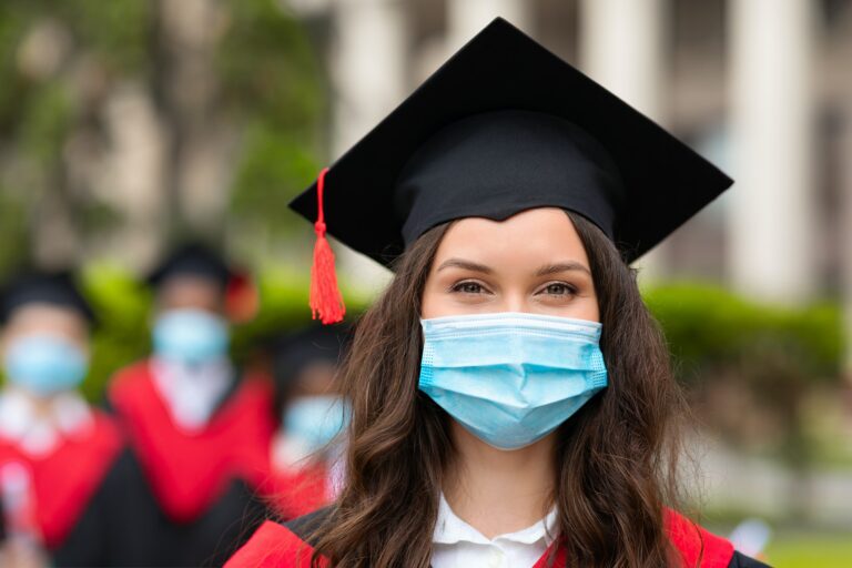 Young brunette lady in graduation costume and face mask, closeup