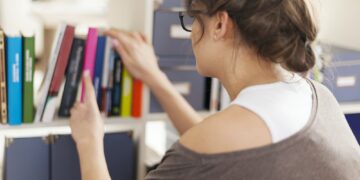 Woman choosing favourite book from home library