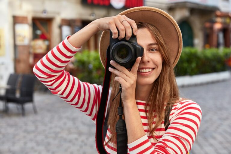 Professional photographer makes amateur photos while strolls in city during excursion, smiles positi