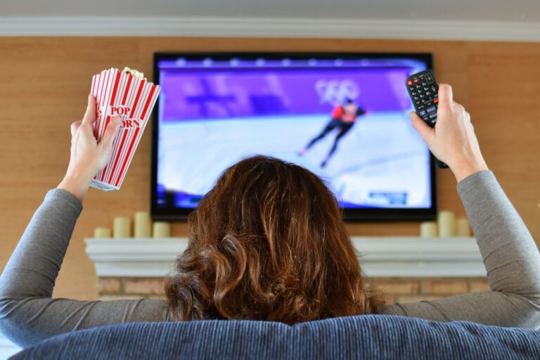 Woman watching sports Olympic speed skating on TV with popcorn and a remote.