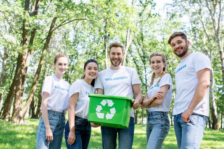 young happy volunteers with green recycling box in park
