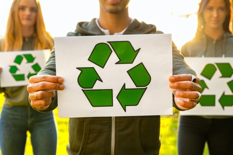 Young volunteers holding recycling symbol placard outdoor
