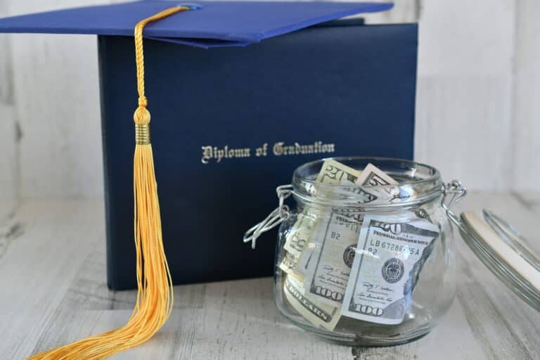 Graduation cap mortarboard tassel on diploma by a jar of money cash, concept school loans debt