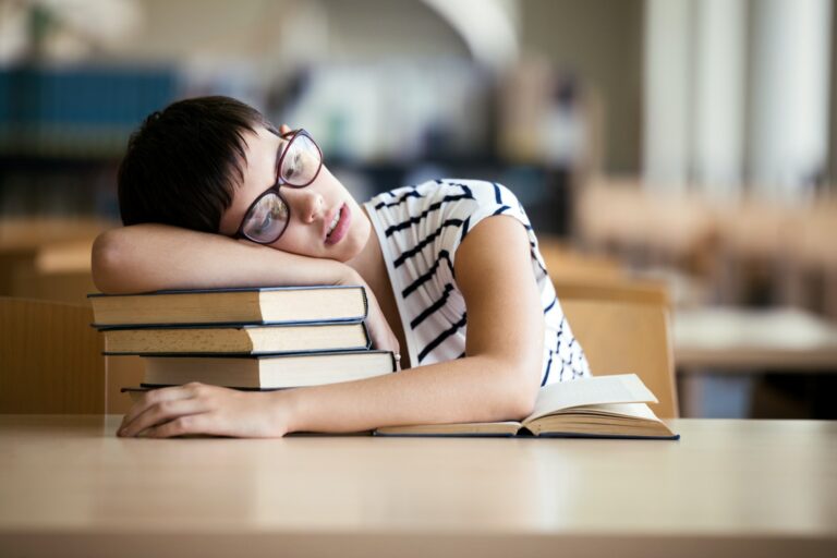 Tired student girl with glasses sleeping on the books