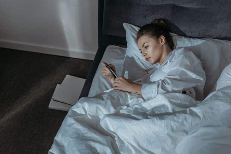 young woman using phone in bed