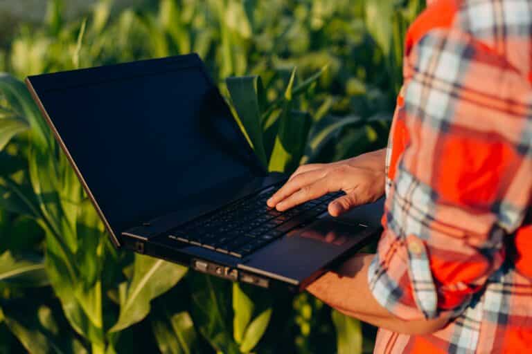 Closeup laptop screen in a male hands. Agronomy standing in a field holding open notebook