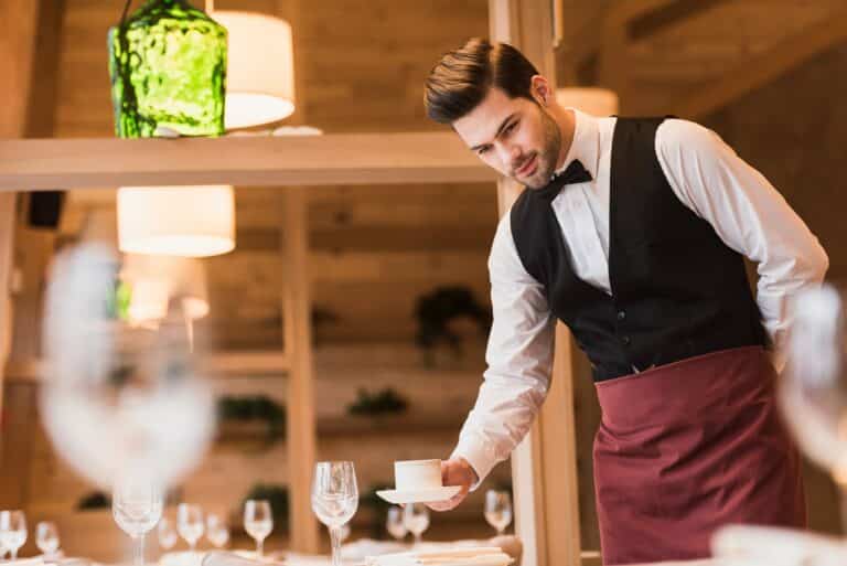 Handsome waiter serving cup of coffee on a table