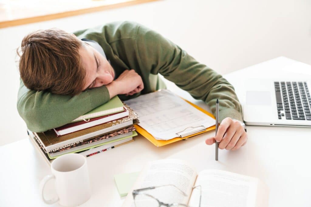 Student at the table indoors sleeping on books.