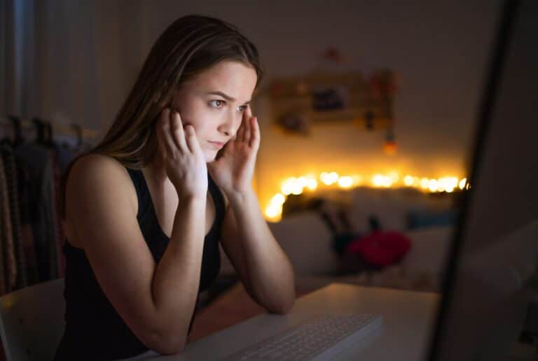 Worried young girl with computer sitting indoors, internet abuse concept