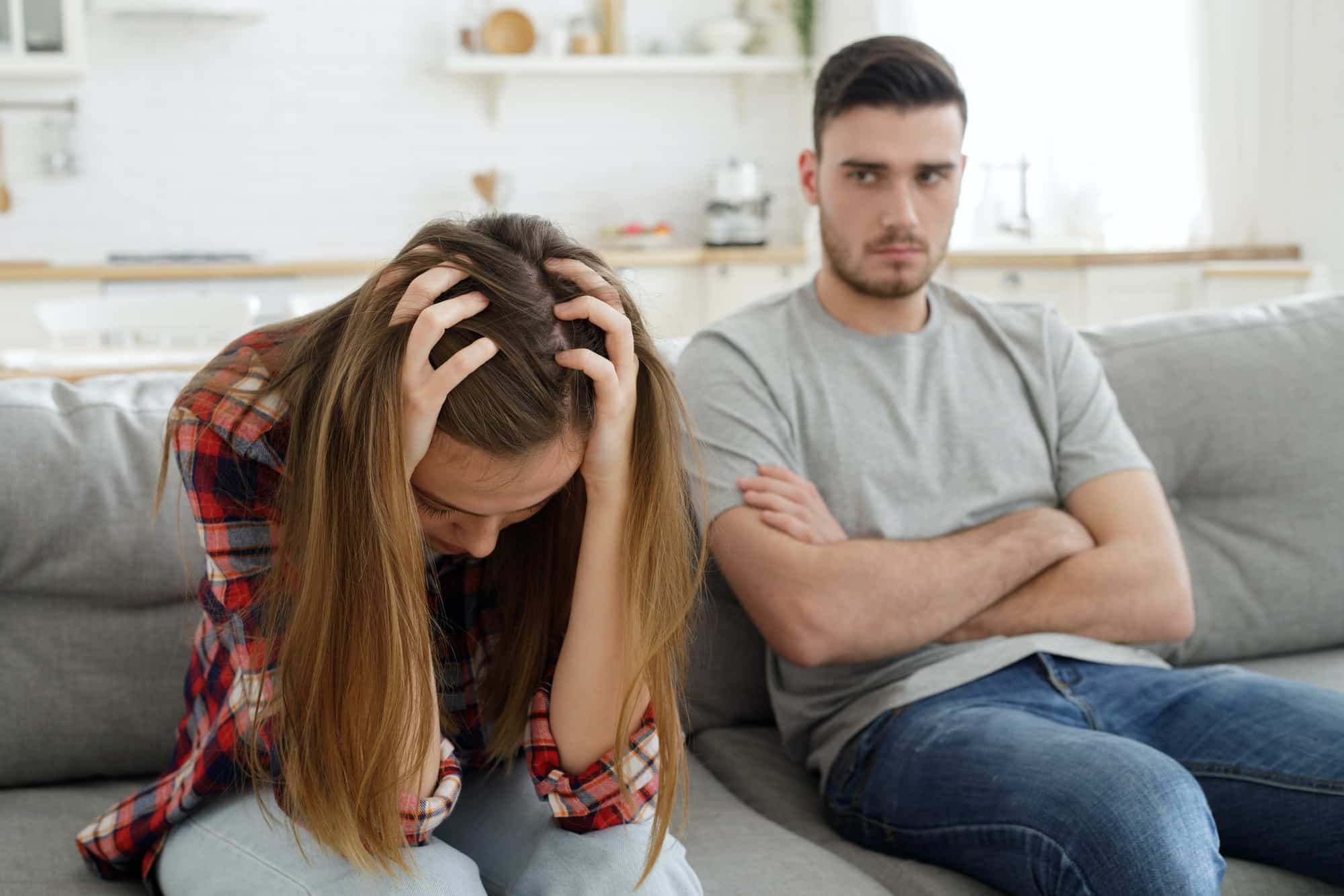 Arguing annoyed young couple sits on couch at home after major breakdown