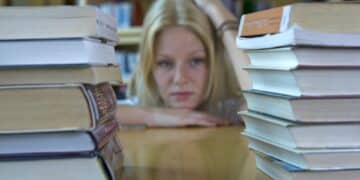 Germany, Baden-Wuertemberg, stressed young female student with stack of books in a library