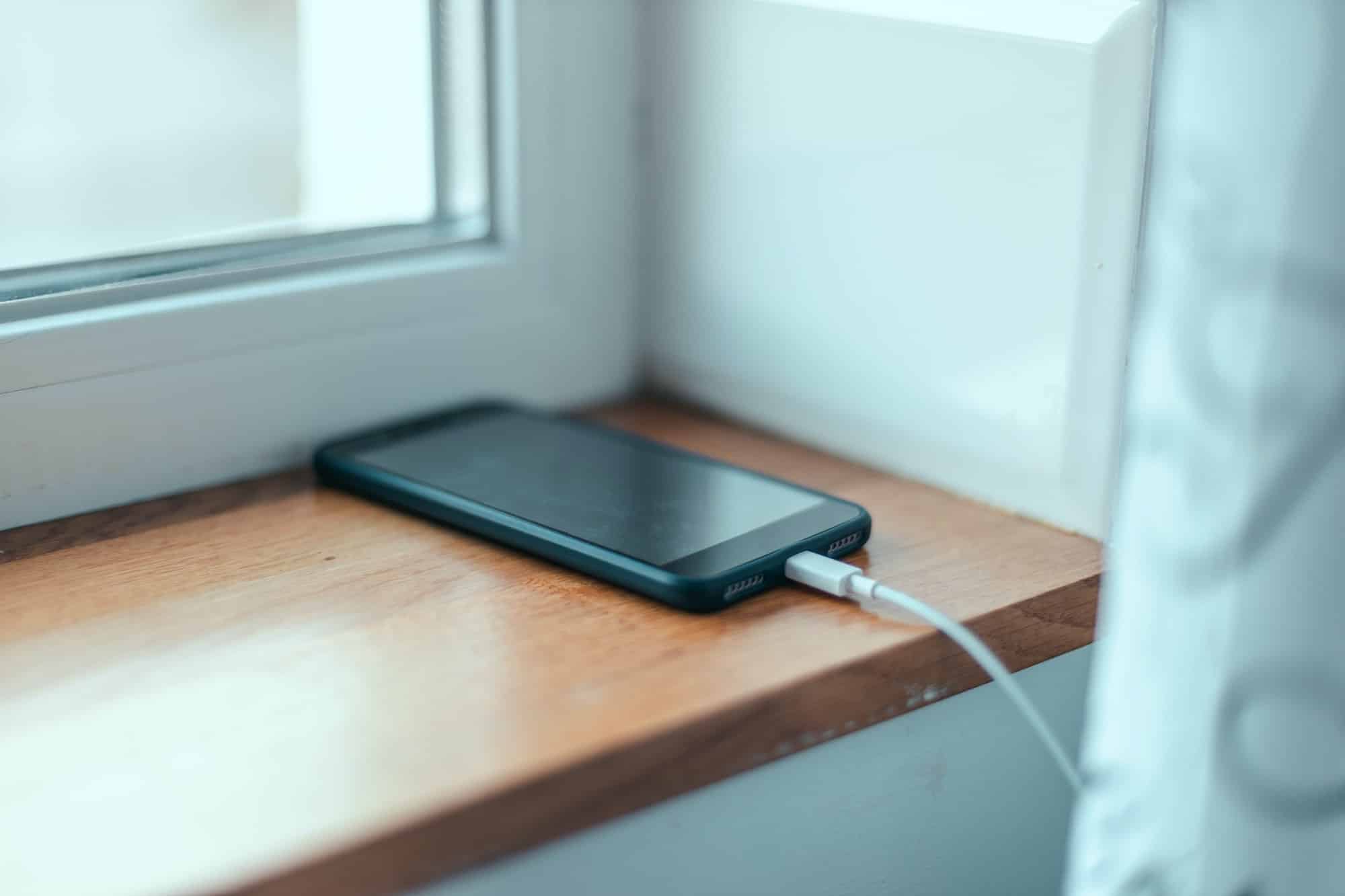 Modern discharged smartphone connected and charging on the windowsill in modern office