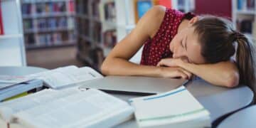 Tired schoolgirl sleeping while studying in library