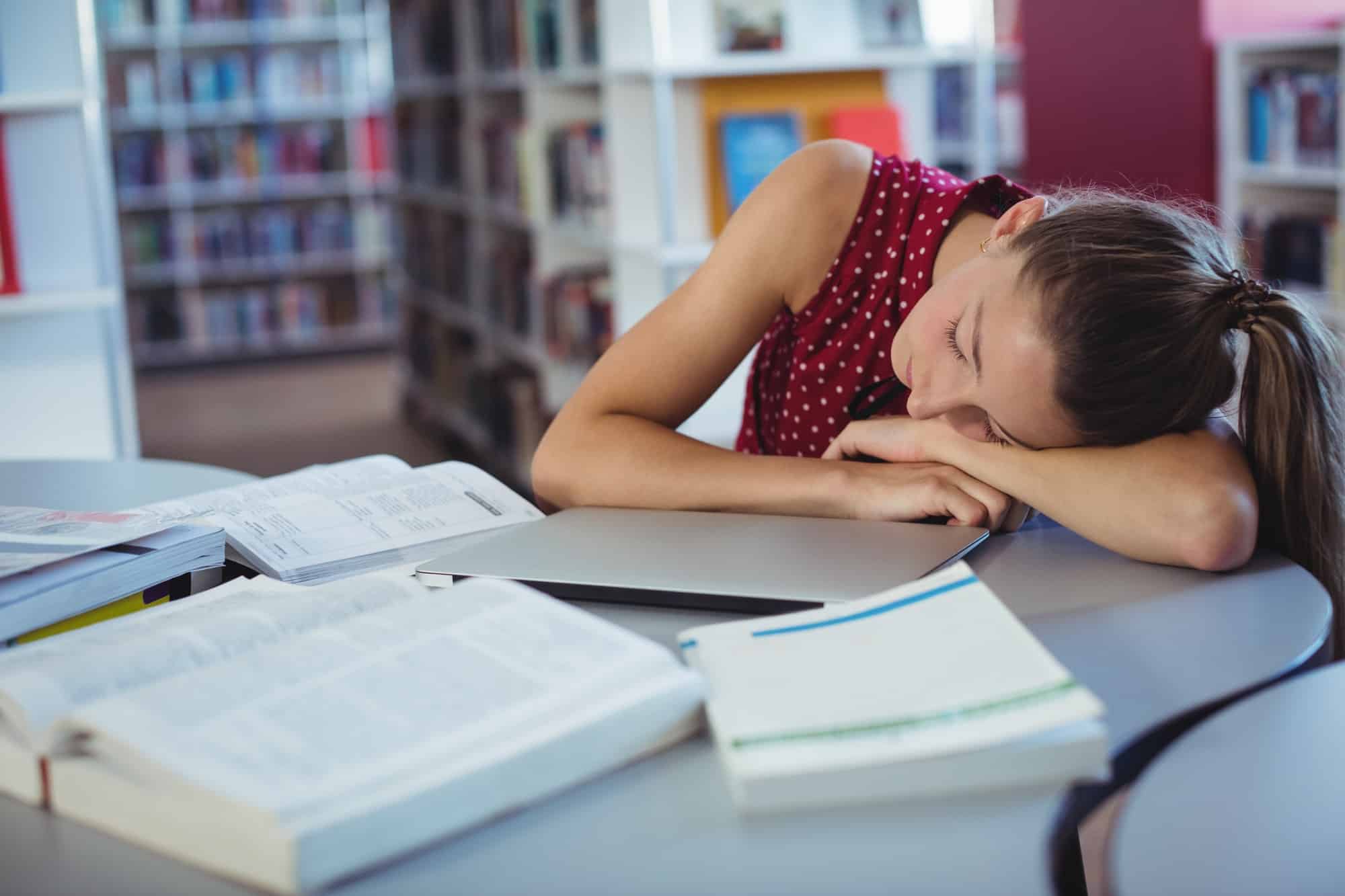 Tired schoolgirl sleeping while studying in library