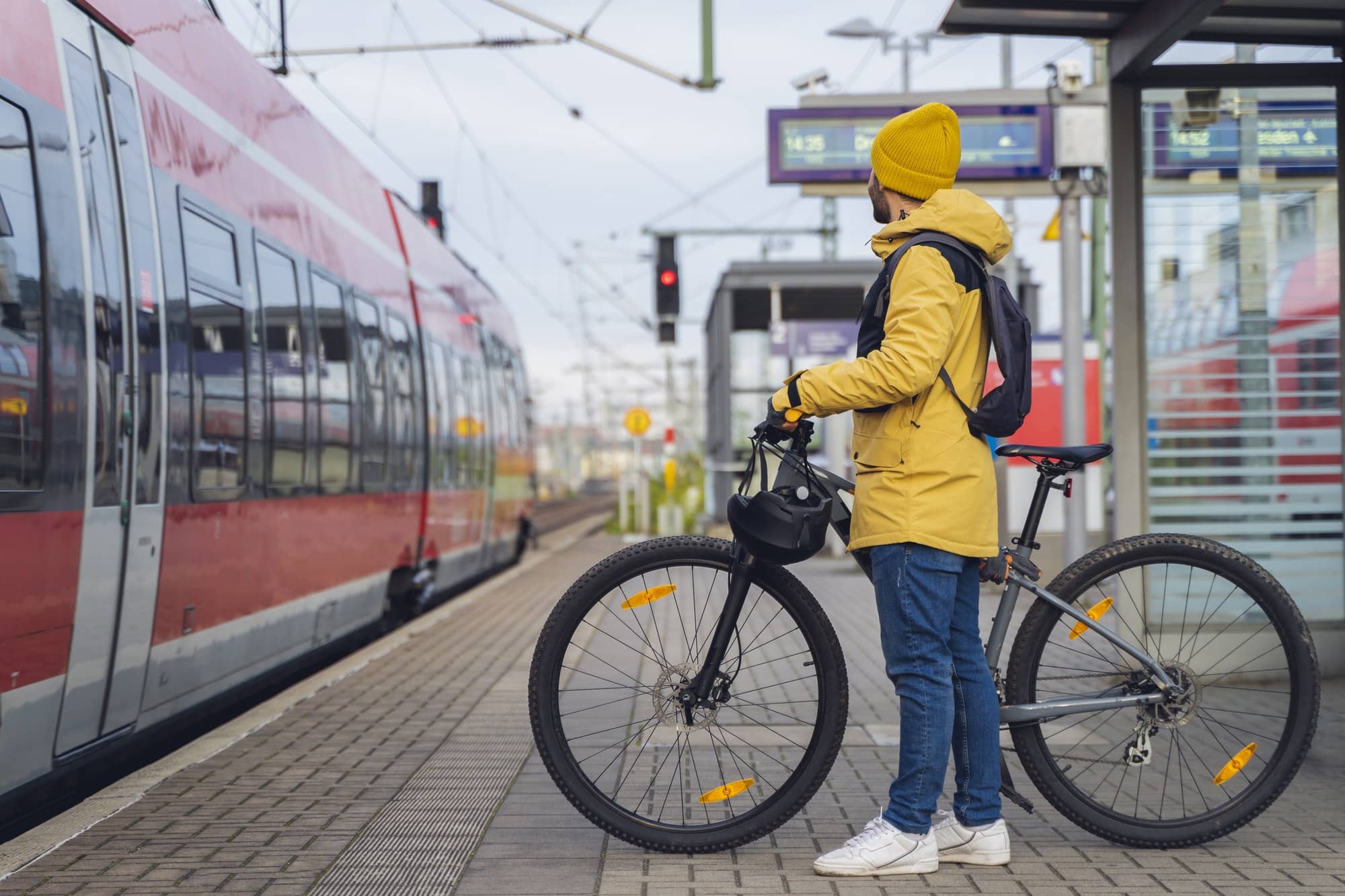 a man wearing winter clothes at the station is about to get on the train with his bicycle