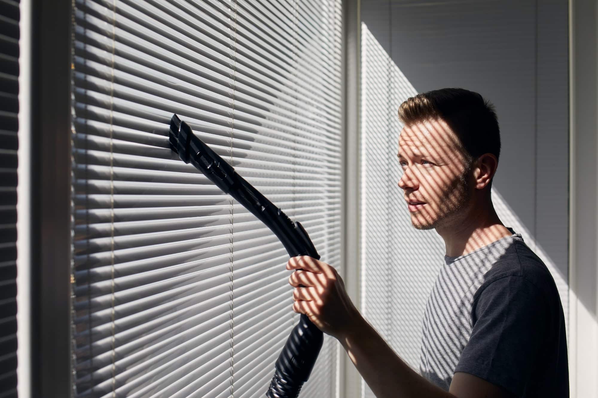 man cleaning dust from window blind by vacuum cleaner