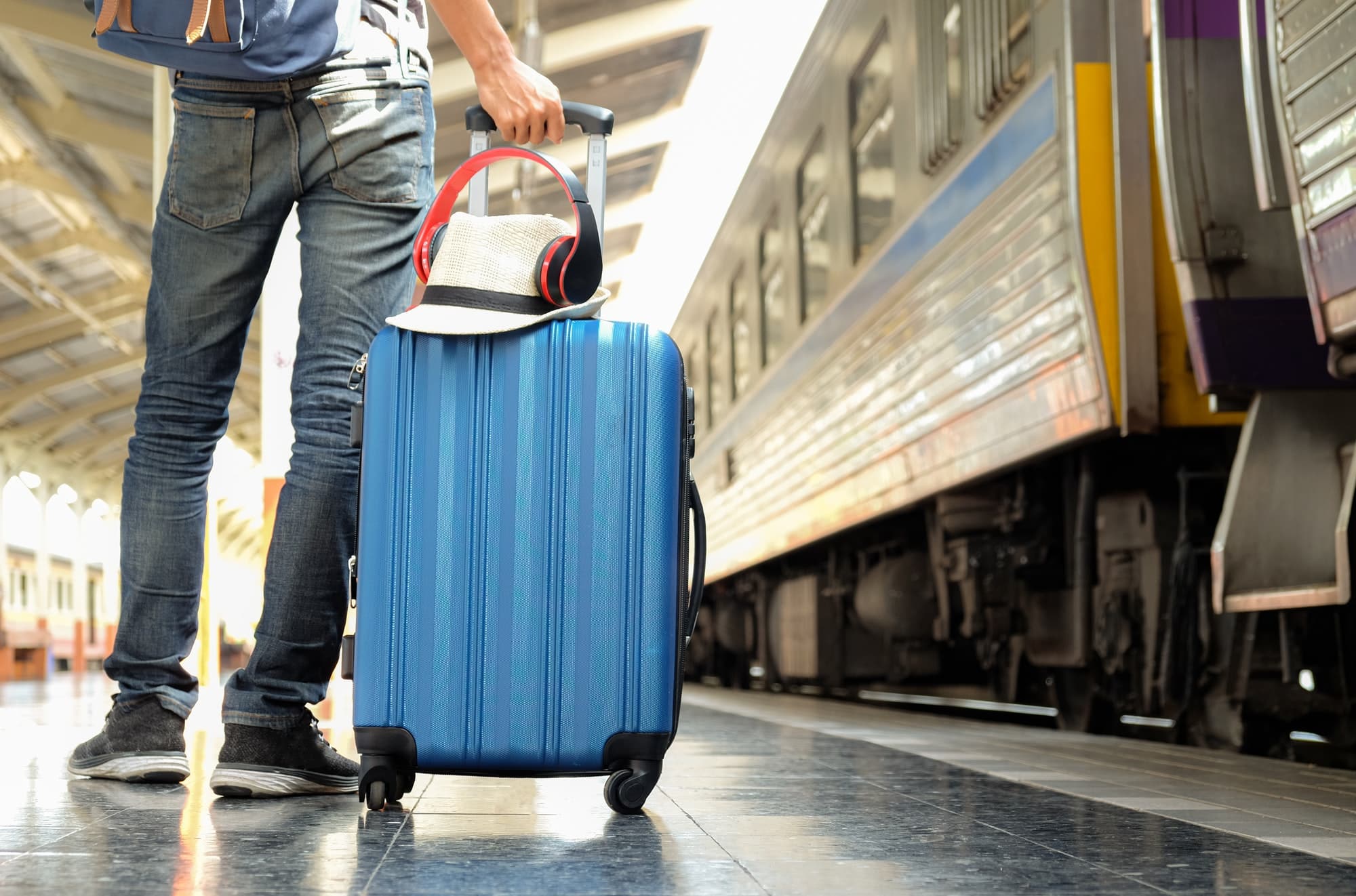 traveler with a blue suitcase is waiting for the train hat and headphone placed on the suitcase