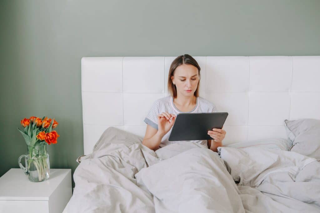 woman in bed with digital tablet in hand surfing internet addiction to online social media