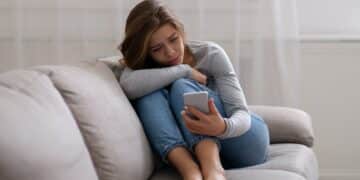 portrait of sad young woman looking at her smartphone suffering from cyber bullying or unhappy