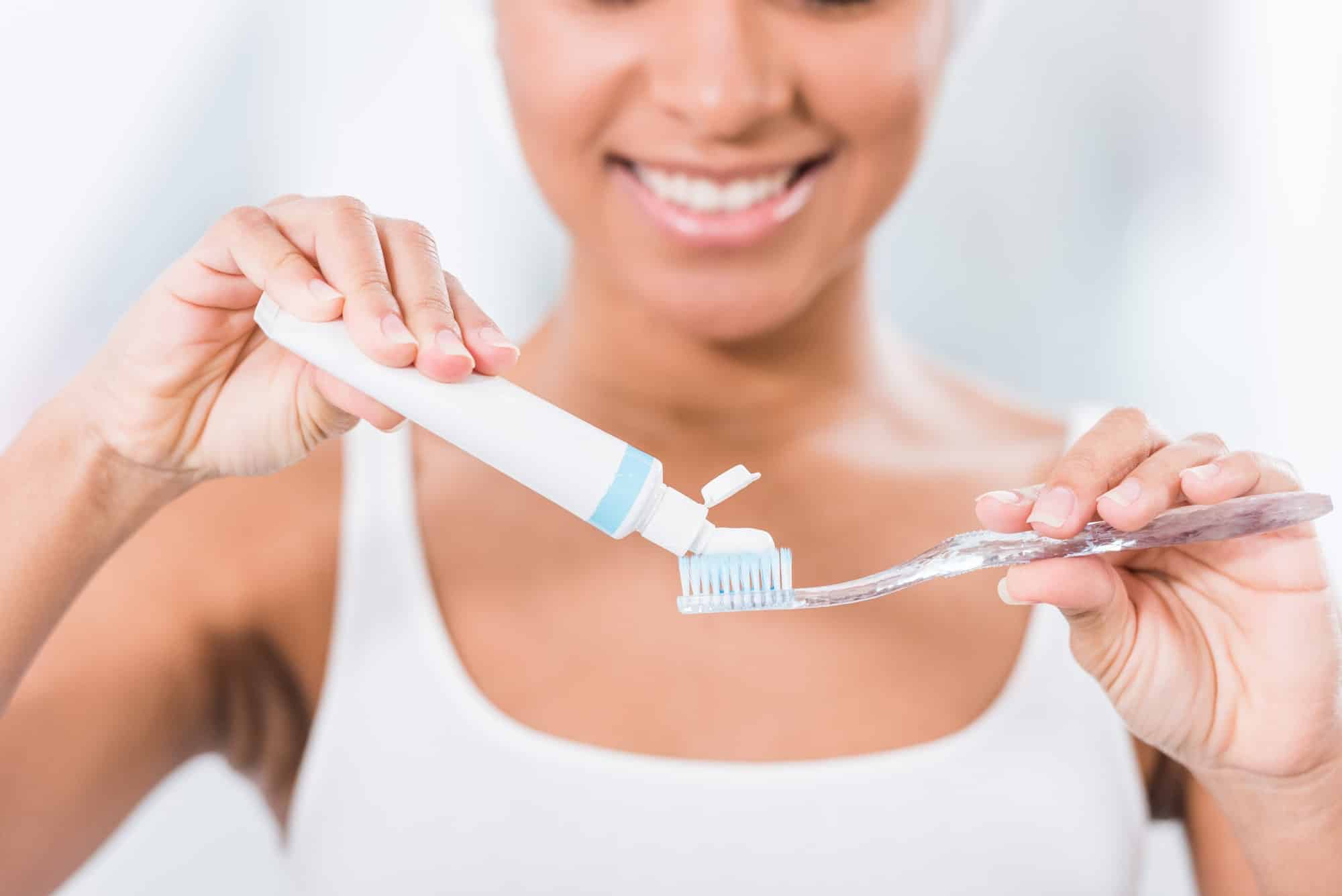 selective focus of young woman putting toothpaste on toothbrush