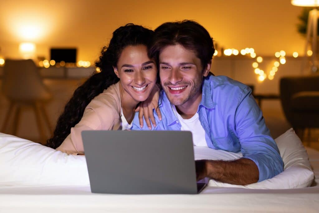 smiling couple using laptop watching funny film in bedroom