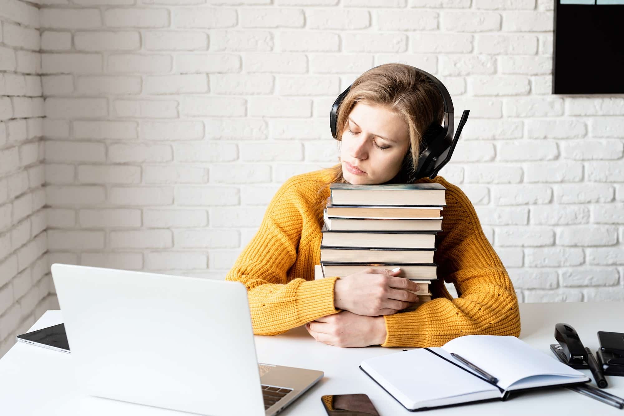 young woman in black headphones sleeping on a stack of books