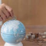 Business woman hand putting one pound coin in to piggy bank for donate money helping the earth,