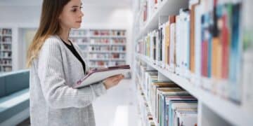 Scholarship, student or woman in library with tablet for research, education or learning. Bookshelf