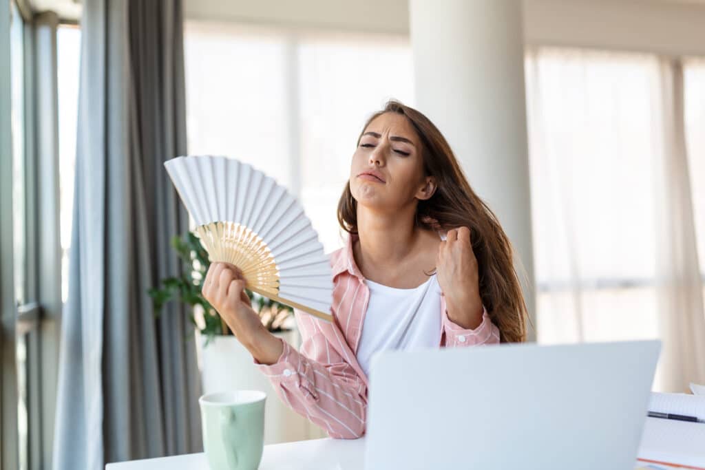 tired overheated young woman hold wave fan suffer from heat sweating indoor work laptop home office annoyed woman feel uncomfortable hot summer weather problem no air conditioner concept