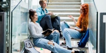 University students sitting on stairs and talking indoors, back to school concept