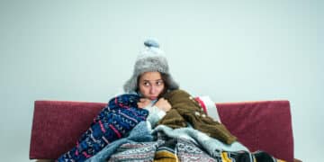 young sick woman with flue sitting sofa home studio covered with knitted warm clothes illness influenza pain concept relaxation home healthcare concepts