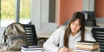 teen girl studying with textbook writing essay learning in classroom